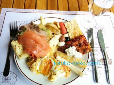 トルコ イスタンブールのポーレンツキョイというところの豪華な朝食。 お皿の上に、サーモン チーズ、ソーセージなどが載っている。フォーク、飲み水、ナイフが添えられている